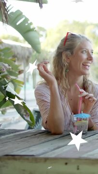 Vertical video: Woman turning to offscreen laugh, laughing and twirling straw, travel stars moving