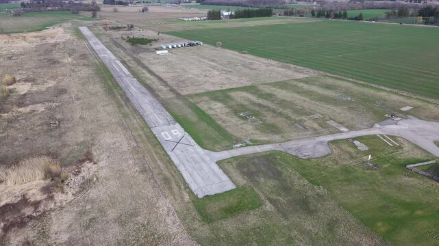 High-angle aerial orbit moving counter-clockwise over the decommissioned runway 09 at Markham Airport, showing cracked asphalt and rural fields