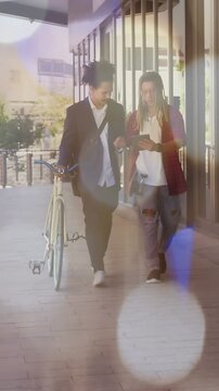 Vertical video: Two men walking, guiding bicycle, tapping tablet, lens flare clearing for tech demo