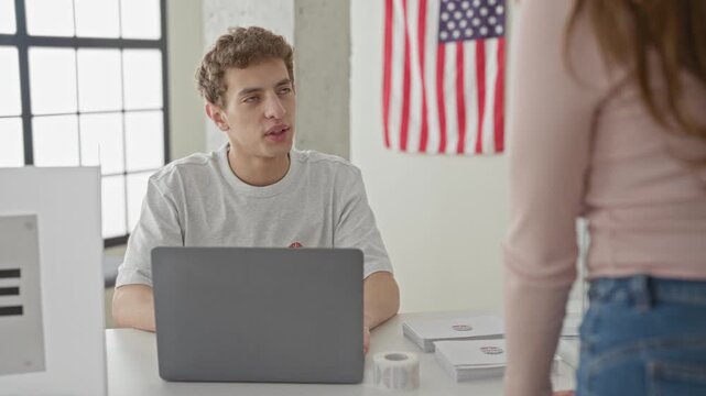 Man at table with laptop hands ballot to woman over clear ballot box in voting building with us flag and registration materials; civic duty responsible.