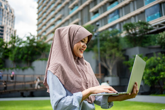 Asian Muslim businesswoman using digital laptop while standing in the city. 
