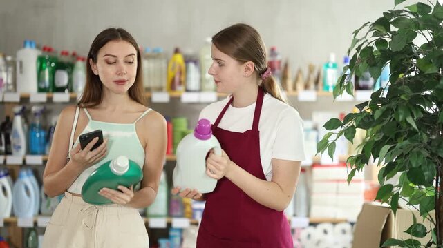  Young woman scanning qr code for laundry detergent with woman seller in household chemicals store 