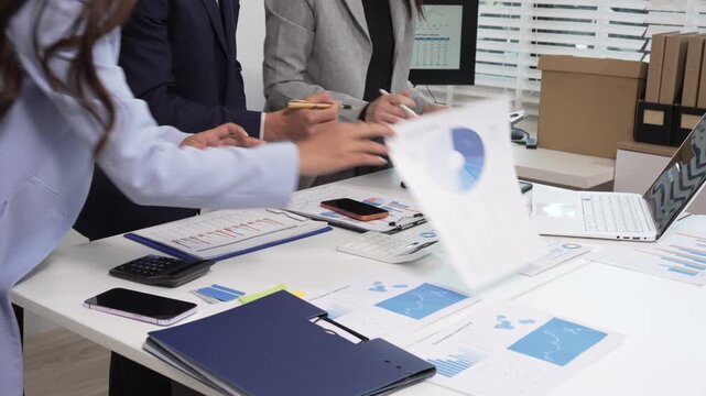 Business team in office reviewing financial reports and charts on desk with laptop, tablet, calculator and documents during meeting.