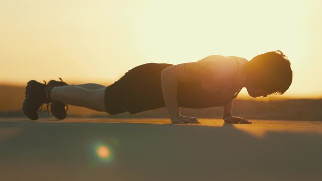 Athletic woman performing push ups during sunset workout