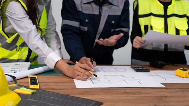 Close-up of architect drafting a floor plan on desk with pencil, ruler and model building, modern office workspace for construction planning and design.