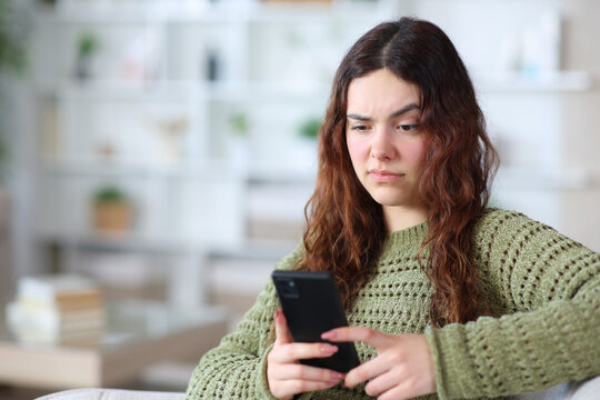 Suspicious young woman checking phone at home