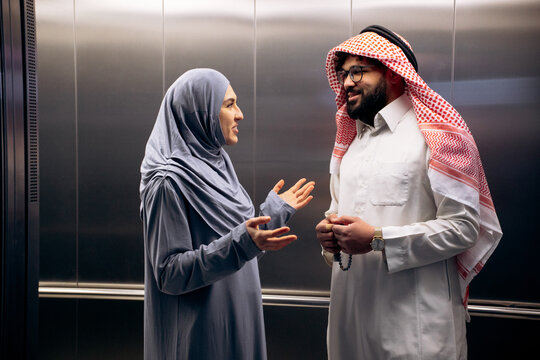 Two diverse muslim business people having a conversation in a modern elevator, discussing work or daily topics