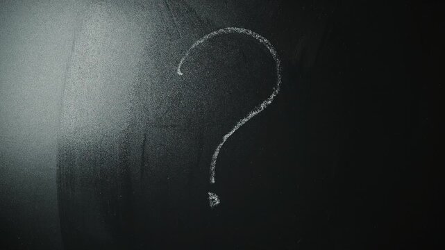 A hand is shown writing a question mark on a chalkboard. This activity takes place in a classroom setting, emphasizing education and inquiry
