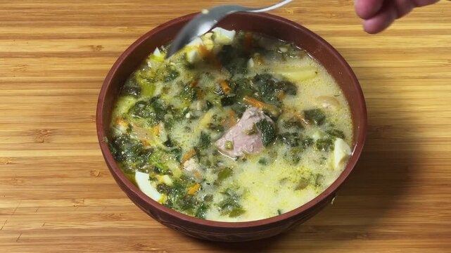 Stirring with spoon of sorrel soup in bowl on wooden surface