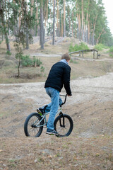 Naklejka premium Young Man Riding BMX Bike on Sandy Forest Trail at Outdoor Bike Park