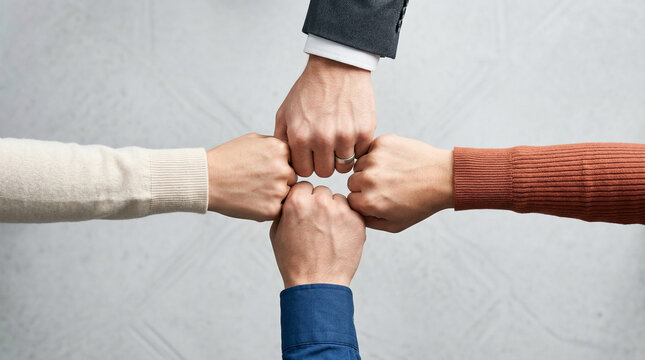 Four diverse hands joined together in unity and teamwork against neutral background