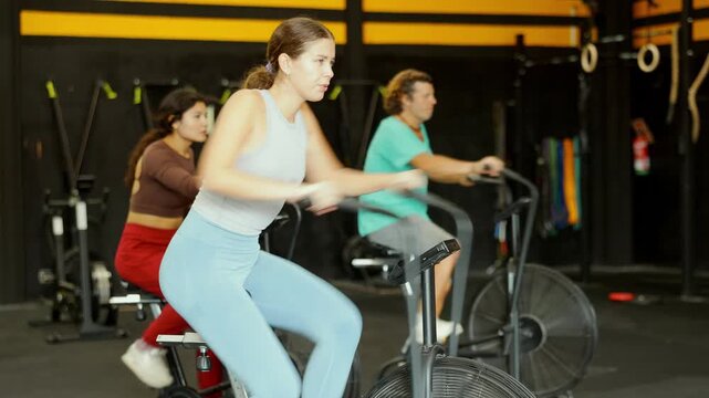 Determined young girl riding air bike in sports hall during crossfit workout. High quality 4k footage