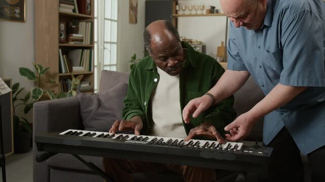 Medium shot of senior African American man learning to play piano at home with mature male teacher helping and correcting hand position Suitable for showcasing personalized education services