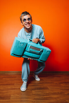 Smiling man with boombox in blue outfit posing against orange wall