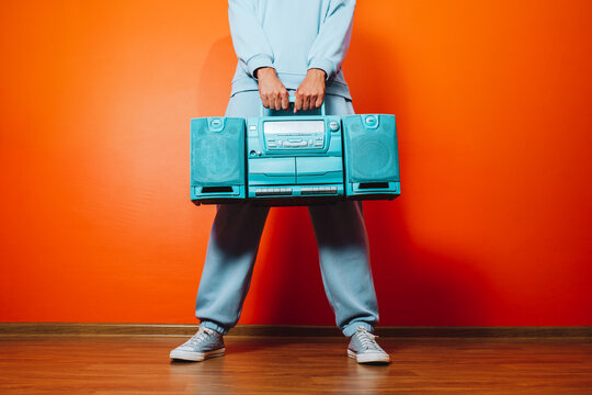 Man in blue tracksuit holding retro boombox against orange wall