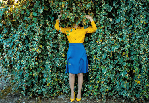 Woman hiding in a green ivy wall merging with surroundings