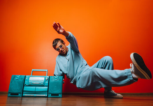 Breakdancer in blue tracksuit posing with retro boombox against orange wall