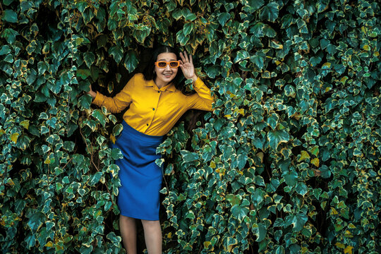 Smiling model in sunglasses hiding in a green ivy wall