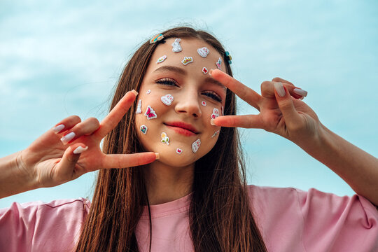 Smiling girl with kawaii face sticker showing peace sign