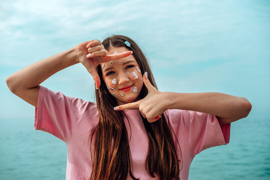 Positive girl with kawaii stickers looking thfrough finger frame by the sea