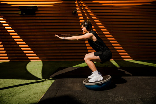 Athlete doing squat on balance equipment outdoors in sunlight