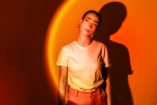 Young woman standing in neon lighting against orange background