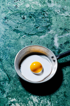 Fake fried egg in small metal pan on green marble background