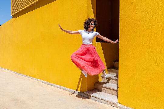 Happy woman with arms outstretched jumping from steps near yellow wall