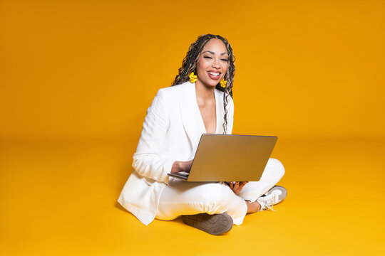 Smiling businesswoman sitting with laptop on yellow background