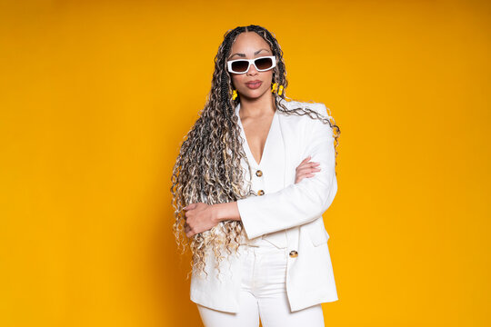 Model in white blazer and sunglasses posing on yellow background