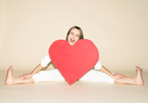 Smiling adult in white jumpsuit holding red paper heart and spreading legs
