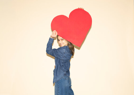 Smiling woman while holding a large red paper heart in jeans outfit