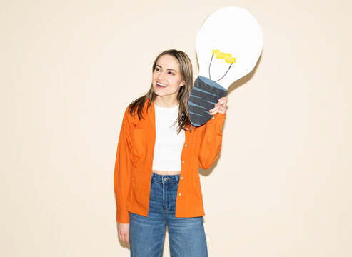 Smiling entrepreneur in orange shirt holding cardboard lightbulb