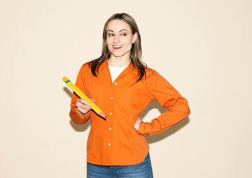 Smiling designer holding large paper pencil for drafting indoors