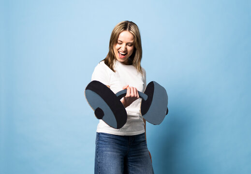 Woman lifting a fake paper dumbbell with effort on a blue background