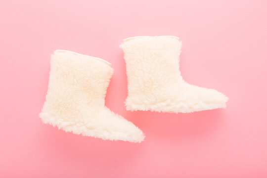 New white warm wool slippers on light pink table background. Pastel color. Female footwear. Closeup. Top down view.