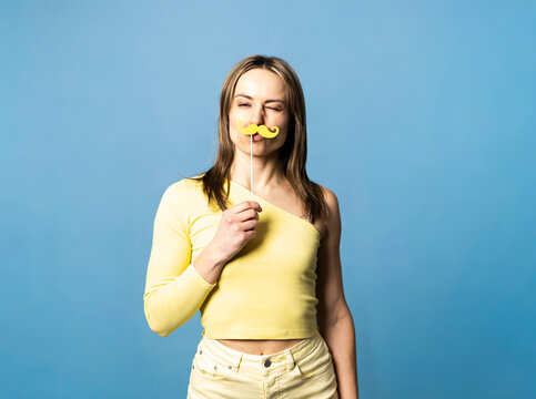 Playful portrait of a woman holding a yellow paper moustache