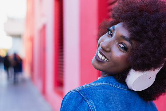 Smiling model with afro listening to music on headphone in city