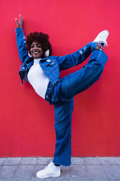 Woman with afro and headphone dancing against red wall