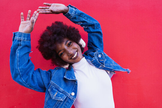 Smiling model with afro enjoying music on a red background