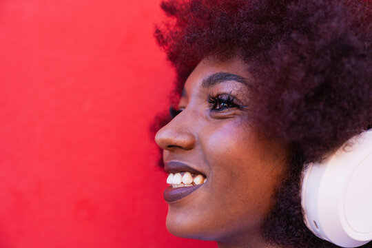 Smiling person with afro listening to music on red background