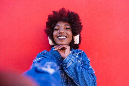 Smiling person taking a selfie with headphone on red background