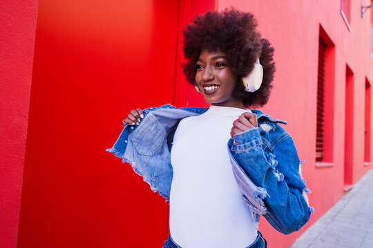 Smiling while listening to music in trendy denim jacket outdoors
