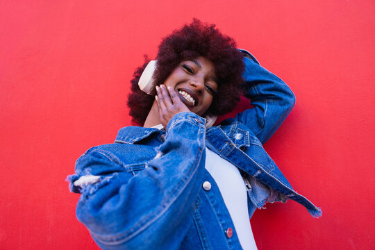Smiling model with afro and headphone on red background