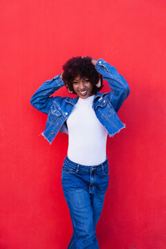 Smiling model listening to music with headphone on red wall