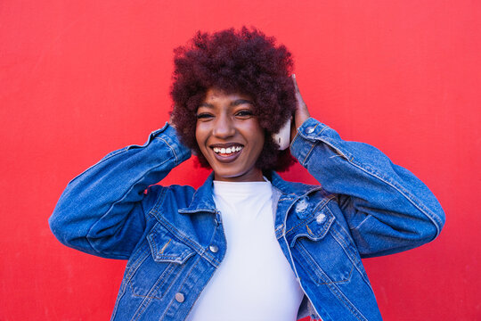 Smiling model listening to music with headphone on red background
