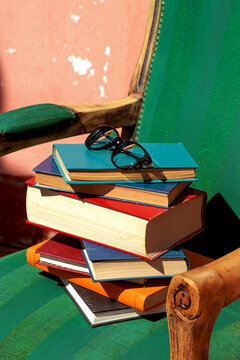 Stack of colorful books with eyewear on a green armchair