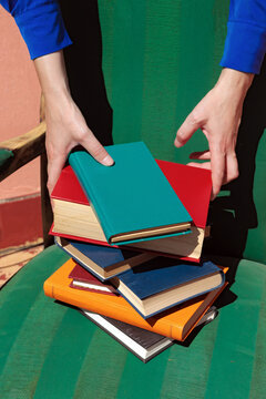 Hands placing a colorful book on a stack in a green armchair