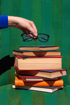 Hand holding eyeglasses over a colorful stack of books