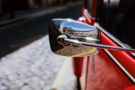 Close up of a chrome side mirror on a red vintage car in the street